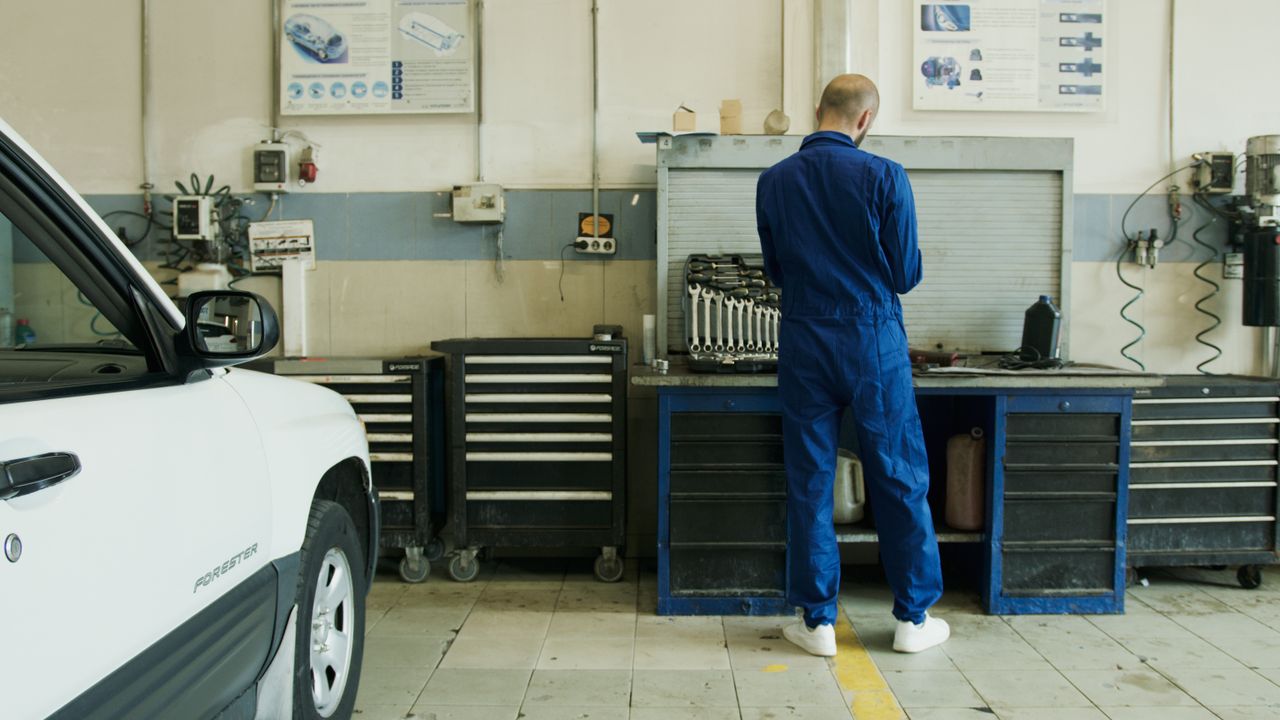 who-we-are Mechanic in blue overalls inspecting a white car in a well-equipped garage.