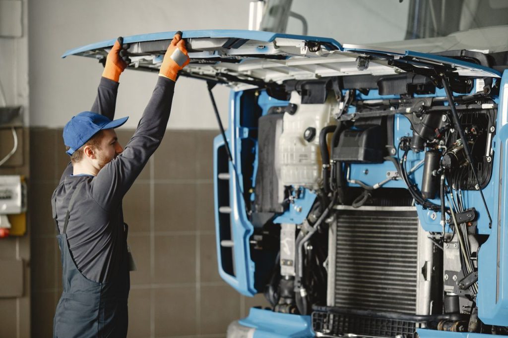 journey Mechanic in uniform inspecting truck engine for maintenance indoors.